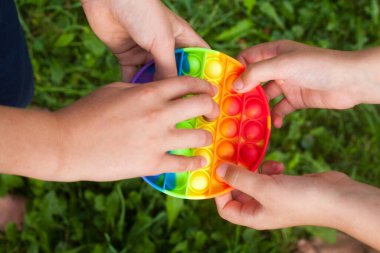 Kids' hands holding round rainbow pop it toy. Playing. New fidget trendy toy. Antistress toy. Simple dimple.
