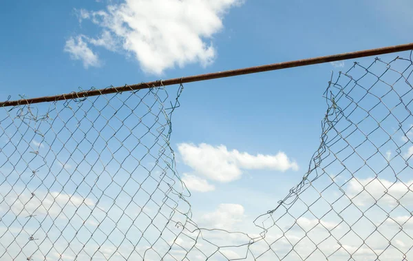 Broken metal mesh fence against the blue sky.