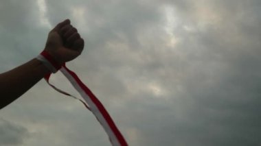 Eller kırmızı ve beyaz kurdele takıyor, gökyüzü arkaplanı, Endonezya bağımsızlık günü konsepti