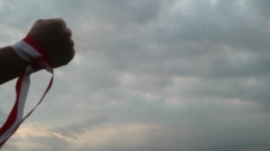 Eller kırmızı ve beyaz kurdele takıyor, gökyüzü arkaplanı, Endonezya bağımsızlık günü konsepti