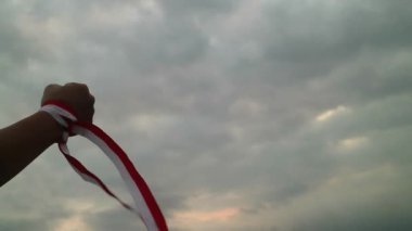Eller kırmızı ve beyaz kurdele takıyor, gökyüzü arkaplanı, Endonezya bağımsızlık günü konsepti