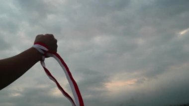 Eller kırmızı ve beyaz kurdele takıyor, gökyüzü arkaplanı, Endonezya bağımsızlık günü konsepti