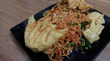 Mie ayam pangsit, tavuklu erişte, hamur tatlısı ve siyah tabakta yemek çubuğu olan sebze, seçici odaklanma..