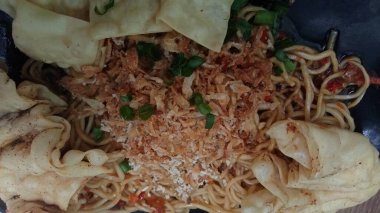 Mie ayam pangsit, tavuklu erişte, hamur tatlısı ve siyah tabakta yemek çubuğu olan sebze, seçici odaklanma..