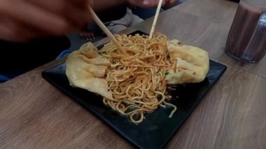 Elleri karıştıran erişteler çubuklarla servis edilen siyah tabakta servis ediliyor.