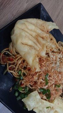 Mie ayam pangsit, tavuklu erişte, hamur tatlısı ve siyah tabakta yemek çubuğu olan sebze, seçici odaklanma..