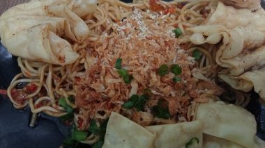 Mie ayam pangsit, tavuklu erişte, hamur tatlısı ve siyah tabakta yemek çubuğu olan sebze, seçici odaklanma..