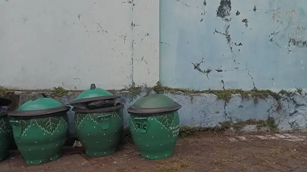 green garbage cans against grey wall, medium shot, copy space