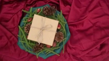 Noel arkaplanı 360 derece dönüş. Firavun yaprakları, kurumuş çam ve kırmızı arka planda dönen hediye kutusu. Yeni yıl hediyeleri, festival ve tatil alışverişi kavramı