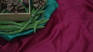 Noel arkaplanı 360 derece dönüş. Firavun yaprakları, kurumuş çam ve kırmızı arka planda dönen hediye kutusu. Yeni yıl hediyeleri, festival ve tatil alışverişi kavramı