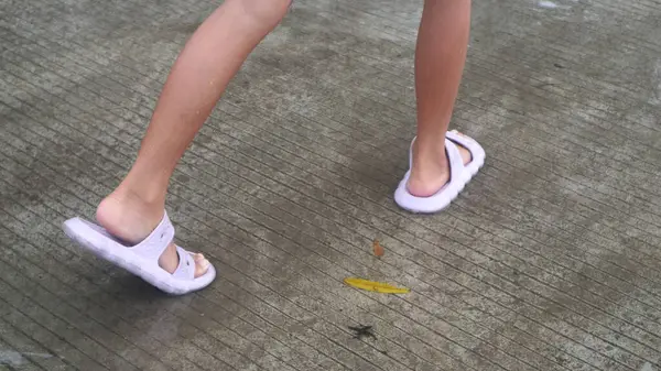 Su birikintilerine basan terlikler giymiş çocukların ayakları.