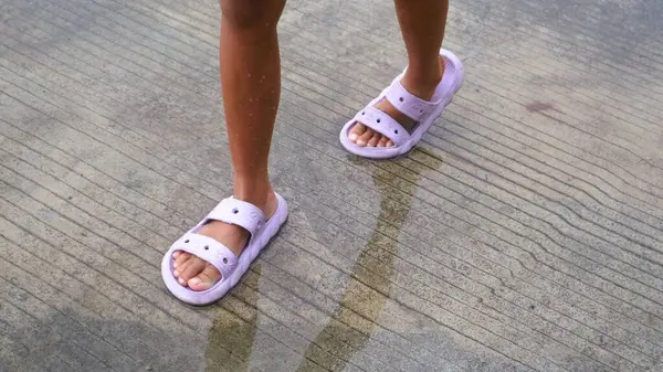 Su birikintilerine basan terlikler giymiş çocukların ayakları.