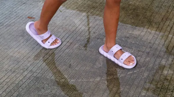 Su birikintilerine basan terlikler giymiş çocukların ayakları.