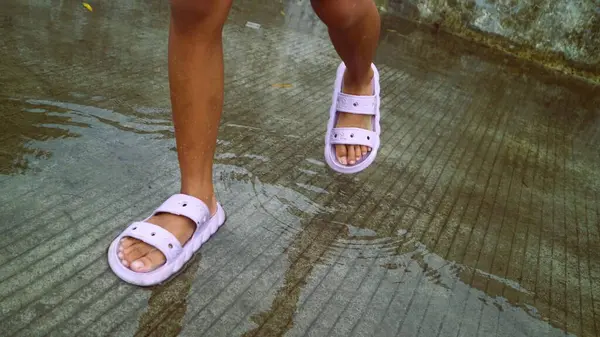 Su birikintilerine basan terlikler giymiş çocukların ayakları.