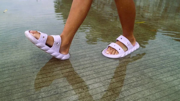 Su birikintilerine basan terlikler giymiş çocukların ayakları.