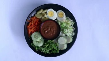 Bir tabakta servis edilen Gado-gado, izole edilmiş beyaz, haşlanmış sebze ve patates içeren Endonezya salatası, haşlanmış yumurta, kızarmış tofu tempeh, lontong ve melinjo cipsi, fıstık-kaju sosuyla servis edilir..