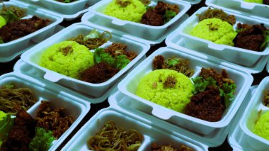 Büyük miktarda sarı pirinç, erişte ve köpüklü yiyecek kabında servis edilen ızgara tavuk paketleri.