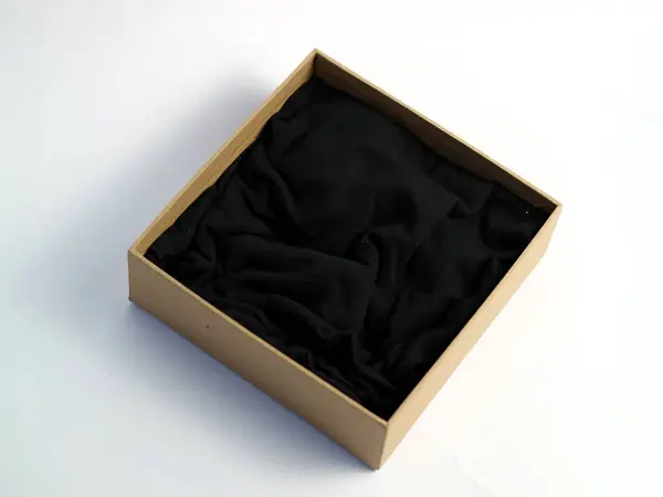 Bir minimalist, içinde siyah kumaş olan karton hediye kutusunu açtı. Ürün fotoğrafçılığı için, el değmemiş beyaz bir arka planda izole edilmiş, kopyalama alanı.