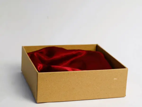Bir minimalist, içinde kırmızı bez bulunan karton hediye kutusunu açtı. Ürün fotoğrafçılık tabanı için. El değmemiş beyaz bir arka planda izole edilmiş.