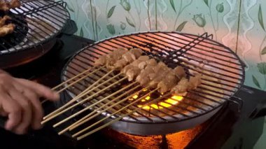 Sate Ayam 'ın 4K görüntüsü, klasik bir Endonezya yemeği olan ızgara tavuk satay, közde pişirilmiş tavuk, dilimlenmiş soğan, fıstık sosu ve biberle servis ediliyor. İkonik bir Endonezya sokak yemeği, lezzetli bir yemek.