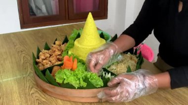 Endonezyalı bir kadın geleneksel sarı pirinç konisi ya da tümör, geleneksel Java mirası mutfağı, Tumpeng nasi kuning üzerine sanatsal düzenlemeler yapıyor ve süslüyor.