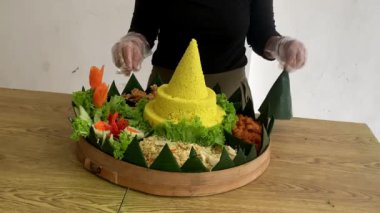 Endonezyalı bir kadın geleneksel sarı pirinç konisi ya da tümör, geleneksel Java mirası mutfağı, Tumpeng nasi kuning üzerine sanatsal düzenlemeler yapıyor ve süslüyor.