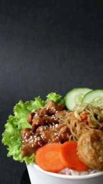 İçinde teriyaki tavuğu, pilav, sebze, erişte, patates püresi ve izole edilmiş siyah arkaplan bulunan döner pirinç kasesi. Öğrencilere uygun basit besleyici yiyecekler ve yoğun öğle yemekleri.. 