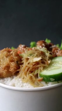 İçinde teriyaki tavuğu, pilav, sebze, erişte, patates püresi ve izole edilmiş siyah arkaplan bulunan döner pirinç kasesi. Öğrencilere uygun basit besleyici yiyecekler ve yoğun öğle yemekleri.. 