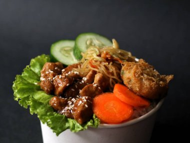 Teriyaki glazed chicken rice bowl with vegetables, noodle, sliced cucumber and wortel and mashed potatoes on black background.  clipart