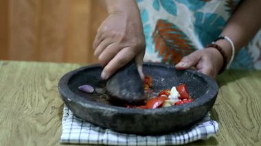 Endonezyalı bir kadının elleri sambal için taş bir havanda baharat öğütüyor. Geleneksel Endonezya sambali havan ve tokmakla hazırlanıyor. Asyalı kadınların elleri biber ve baharatları öğütücüde eziyor. 4K görüntü