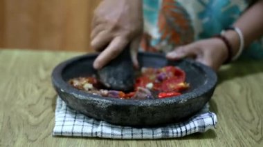 Endonezyalı bir kadının elleri sambal için taş bir havanda baharat öğütüyor. Geleneksel Endonezya sambali havan ve tokmakla hazırlanıyor. Asyalı kadınların elleri biber ve baharatları öğütücüde eziyor..