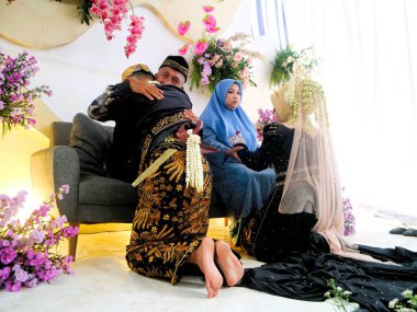 Sungkeman is sacred processions in traditional Javanese weddings. The bride and groom kneel before their parents to ask for blessings and prayers. Couple wearing traditional Javanese clothes during wedding ceremony clipart