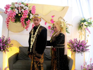 Sungkeman is sacred processions in traditional Javanese weddings. The bride and groom kneel before their parents to ask for blessings and prayers. Couple wearing traditional Javanese clothes during wedding ceremony clipart