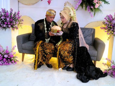 Sungkeman is sacred processions in traditional Javanese weddings. The bride and groom kneel before their parents to ask for blessings and prayers. Couple wearing traditional Javanese clothes during wedding ceremony clipart