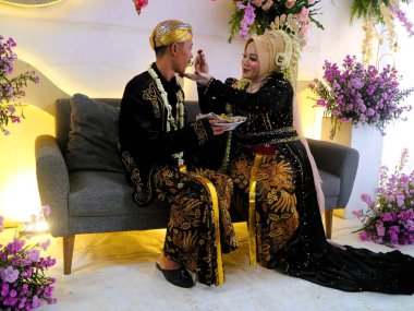 Sungkeman is sacred processions in traditional Javanese weddings. The bride and groom kneel before their parents to ask for blessings and prayers. Couple wearing traditional Javanese clothes during wedding ceremony clipart