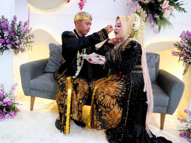 Sungkeman is sacred processions in traditional Javanese weddings. The bride and groom kneel before their parents to ask for blessings and prayers. Couple wearing traditional Javanese clothes during wedding ceremony clipart