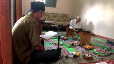 Asyalı Endonezyalı erkekler sarong ve peci giyip oturma odasında Kur 'an okuyorlar, Müslümanlar için dini günlük keskinlik.