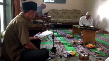 Asyalı Endonezyalı erkekler sarong ve peci giyip oturma odasında Kur 'an okuyorlar, Müslümanlar için dini günlük keskinlik.