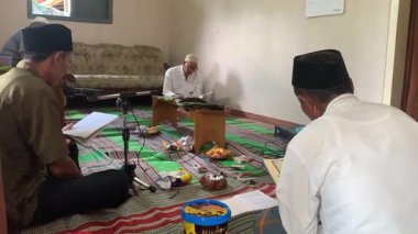Asyalı Endonezyalı erkekler sarong ve peci giyip oturma odasında Kur 'an okuyorlar, Müslümanlar için dini günlük keskinlik.