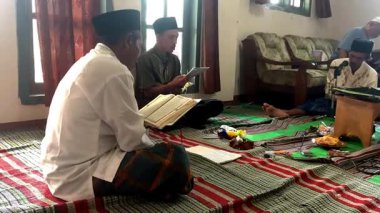 Asyalı Endonezyalı erkekler sarong ve peci giyip oturma odasında Kur 'an okuyorlar, Müslümanlar için dini günlük keskinlik.