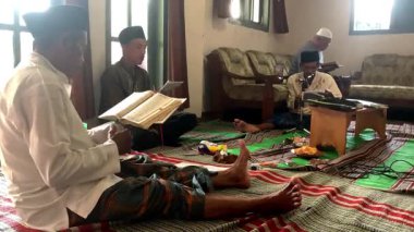 Asyalı Endonezyalı erkekler sarong ve peci giyip oturma odasında Kur 'an okuyorlar, Müslümanlar için dini günlük keskinlik.