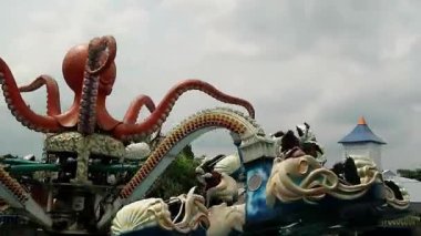 Canlı dokunaçları dönen arabaların üzerinde uzanan ahtapot şeklinde renkli bir lunapark gezisi, mavi gökyüzü arka planı, aile mutluluğu için yolculuk yeri Malang East Java 'daki Jatim Park 2.