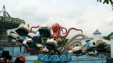 Canlı dokunaçları dönen arabaların üzerinde uzanan ahtapot şeklinde renkli bir lunapark gezisi, mavi gökyüzü arka planı, aile mutluluğu için yolculuk yeri Malang East Java 'daki Jatim Park 2.