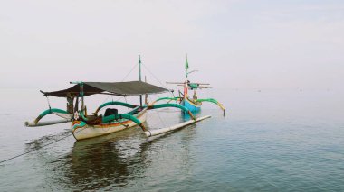 Sahil kıyısında açık gri gökyüzü arka planıyla renkli bir balıkçı teknesi.