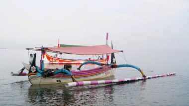 Sahil kıyısında açık gri gökyüzü arka planıyla renkli bir balıkçı teknesi.