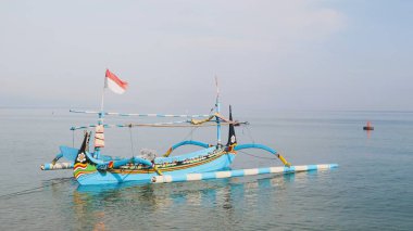 Sahil kıyısında açık gri gökyüzü arka planıyla renkli bir balıkçı teknesi.