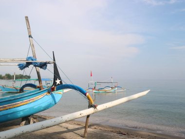 Sahil kıyısında açık gri gökyüzü arka planıyla renkli bir balıkçı teknesi.