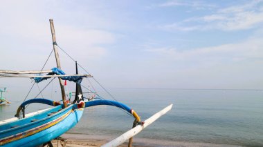 Sahil kıyısında açık gri gökyüzü arka planıyla renkli bir balıkçı teknesi.