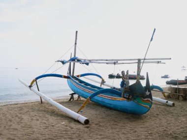 Sahil kıyısında açık gri gökyüzü arka planıyla renkli bir balıkçı teknesi.