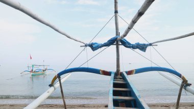 Sahil kıyısında açık gri gökyüzü arka planıyla renkli bir balıkçı teknesi.